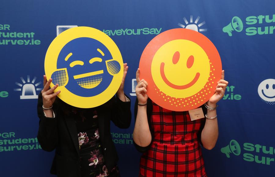 Photograph of two people, each with a cardboard cut out of a smiley face in front of their own face